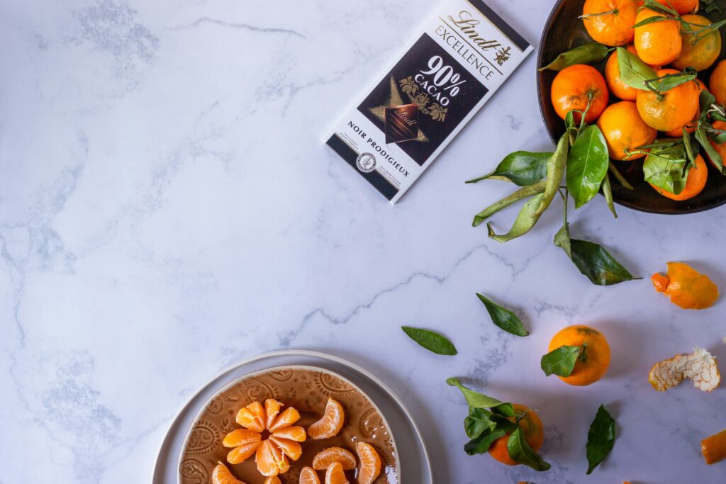 Clémentines et mandarines sur une table en marbre, avec une tablette de chocolat à 90% de cacao, pour gérer son alimentation